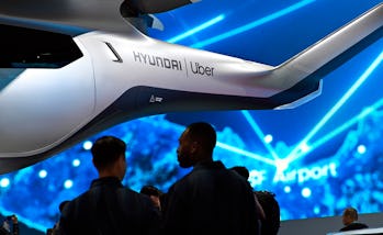 An Uber air taxi is seen suspended at a conference. The background is electric blue. There are two p...