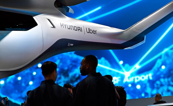 An Uber air taxi is seen suspended at a conference. The background is electric blue. There are two p...