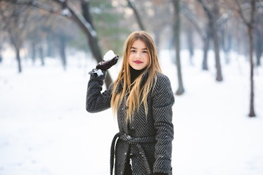 A trendy woman with a peacoat on holds a snowball.