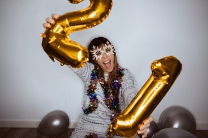A happy woman holds up a two and one balloon while celebrating the new year at home.