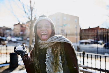 A young Black woman smiles for an Instagram picture, while standing in the city with a snowball on a...