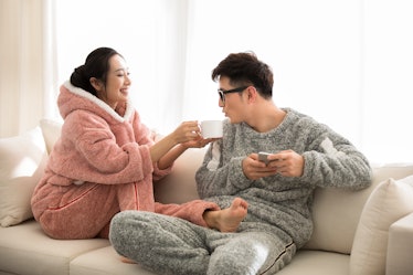 A couple in fuzzy onesies lounge on the couch, sipping warm drinks.
