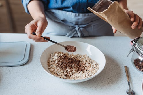 A person wearing a blue apron sprinkles cinnamon on oatmeal. The health benefits of cinnamon are man...