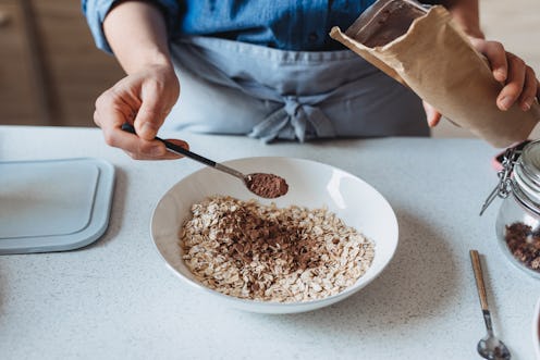 A person wearing a blue apron sprinkles cinnamon on oatmeal. The health benefits of cinnamon are man...