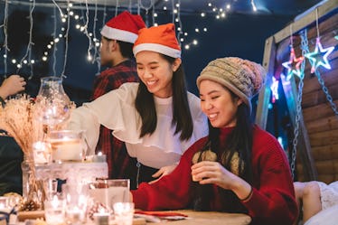 Two friends dressed up for Christmas sit at a table and light Christmas candles.