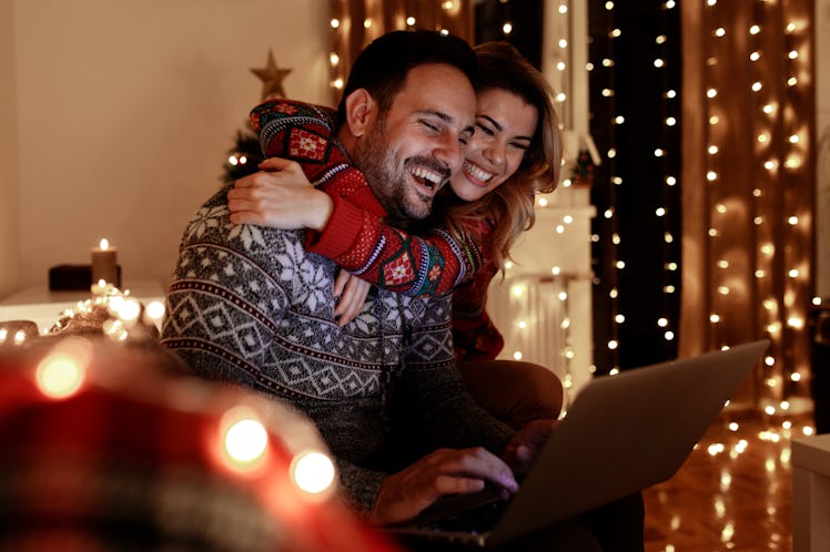 A happy and festive couple embraces while shopping online for the holidays.