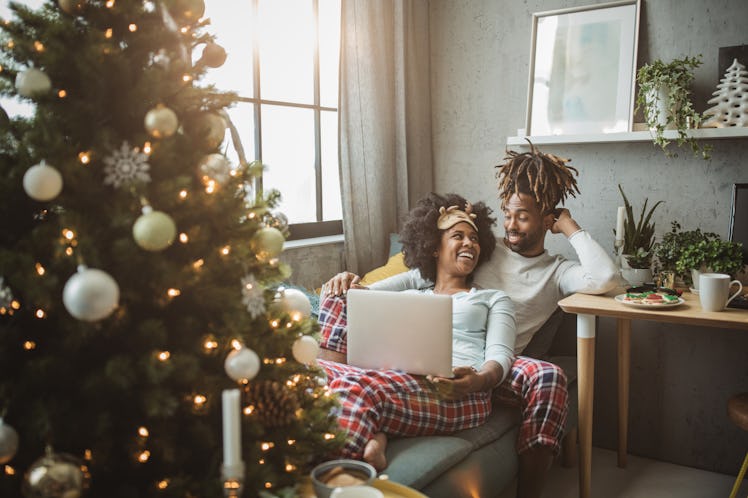 A happy couple in matching Christmas PJs snuggles up on the couch.