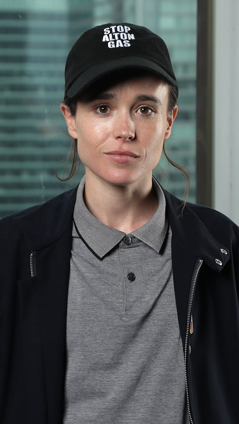 Elliot Page wearing a cap reading ' Stop Alton Gas' and a grey polo shirt with a black jacket.