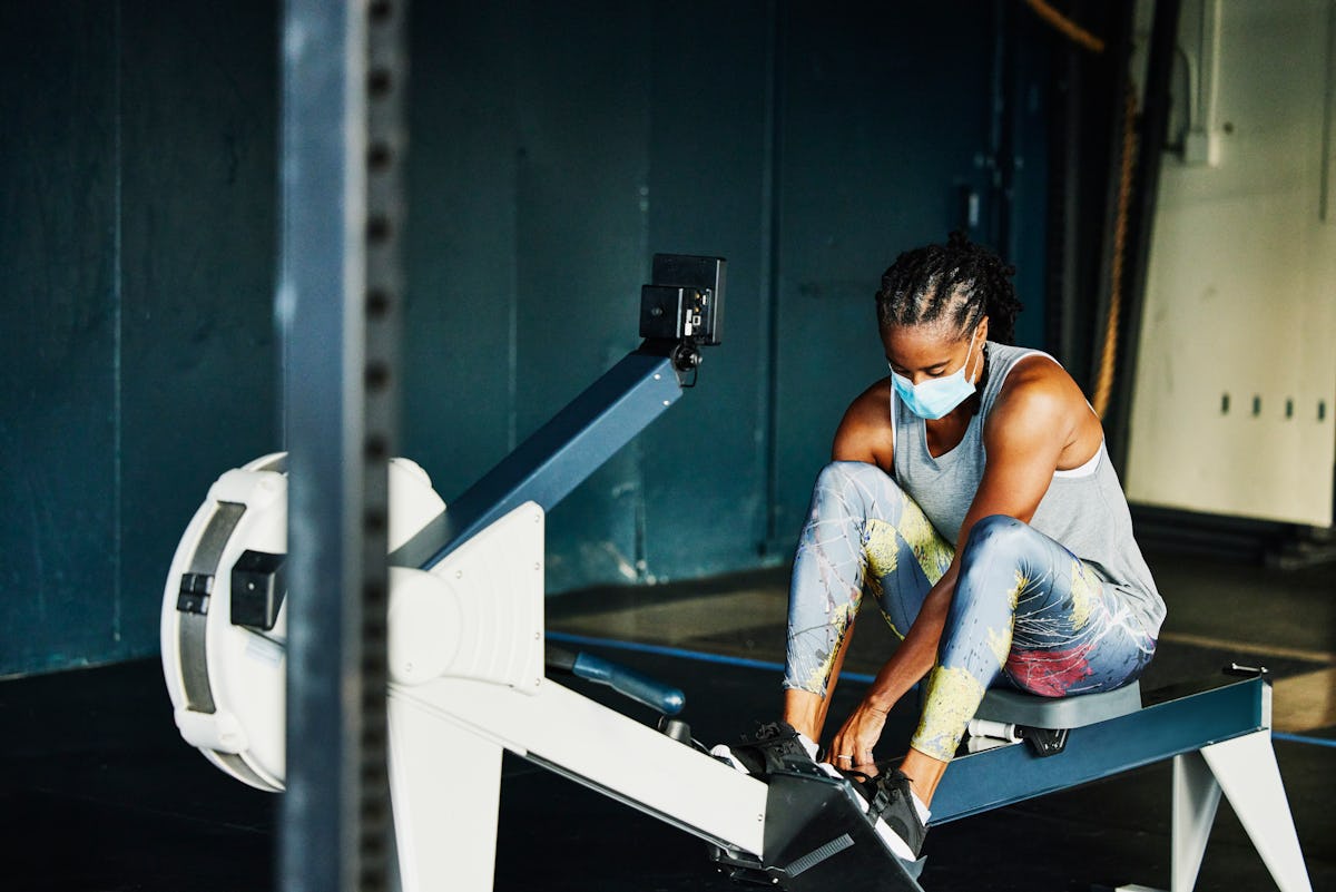 A person wears a mask while setting up to work out on a rower. The new WHO physical activity guideli...