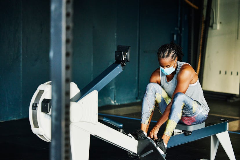 A person wears a mask while setting up to work out on a rower. The new WHO physical activity guideli...