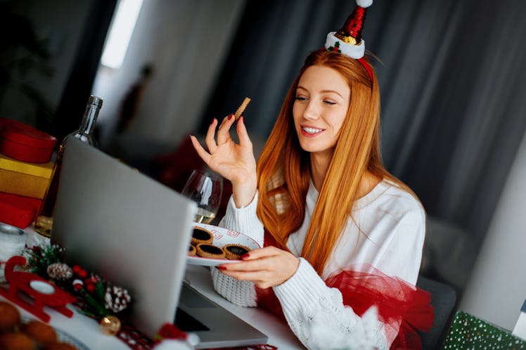 A happy woman wearing a Santa hat holds a plate of Christmas cookies while chatting with friends on ...