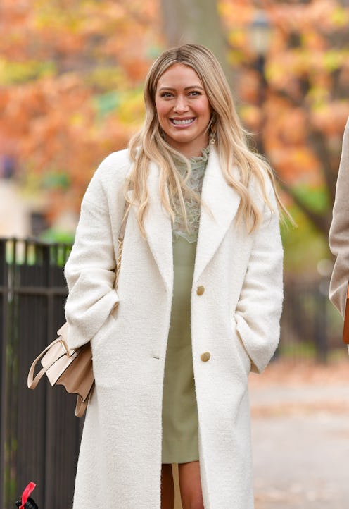 Hilary Duff with a long blonde hair strolling through the park in a white coat