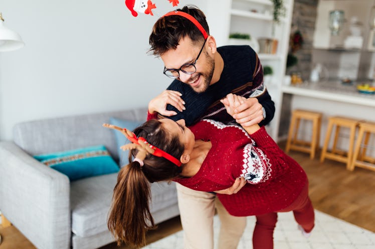 A happy festive couple dances to Christmas music in their home.