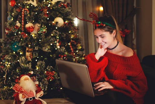 A girl playing games on her laptop next to a Christmas tree