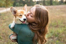 A pet-obsessed brunette woman holding and kissing her corgi dog