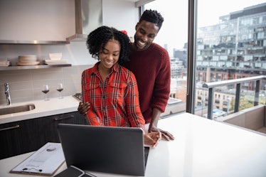 A happy couple looks at their laptop in their bright kitchen.