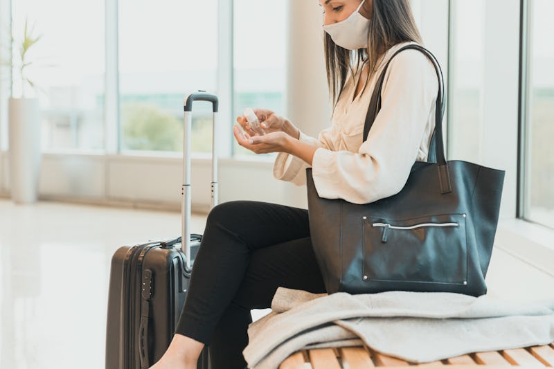 A woman wearing a mask sits at an airport and applies hand sanitizer. Traveling and taking vacations...