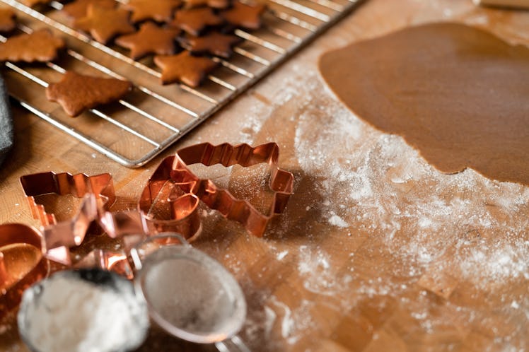Copper cookie cutters sit on a table that's covered with flour and gingerbread dough.