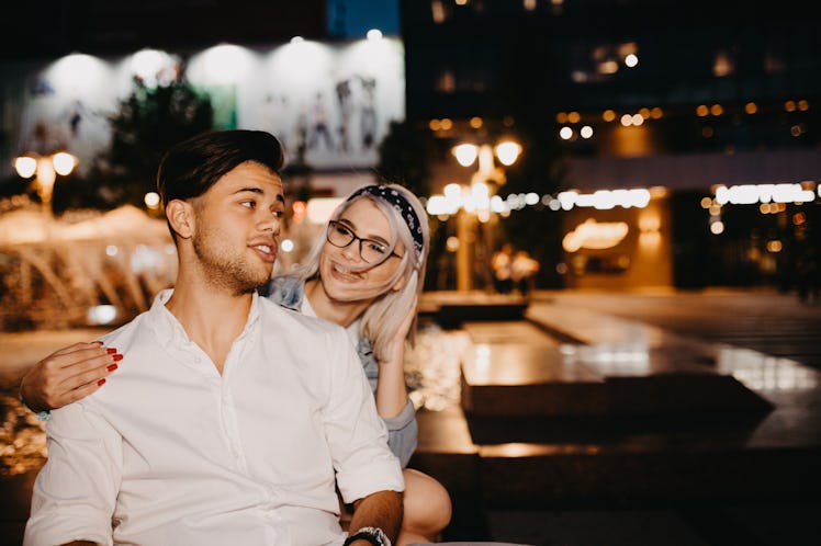 A couple hangs out in the city together, with bright lights glowing in the background. 