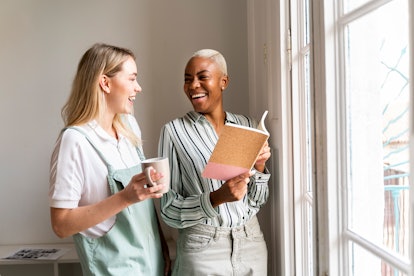 Two women laugh in a sunny room while holding a new journal.