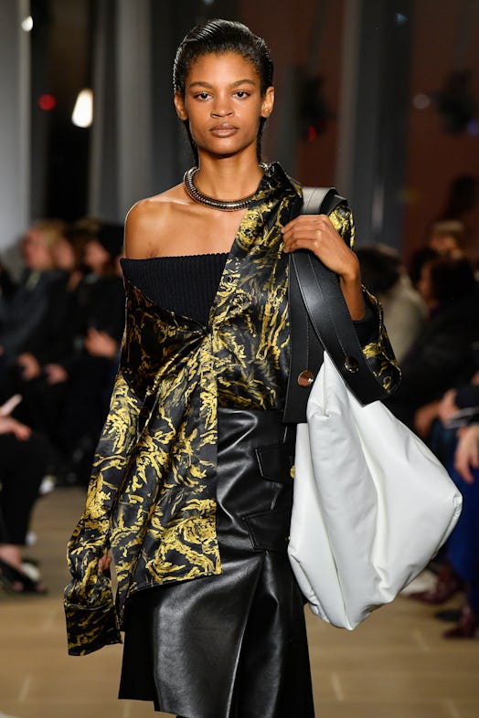 A model in a black leather skirt, a black top paired with a tucked-in shirt with yellow details that...