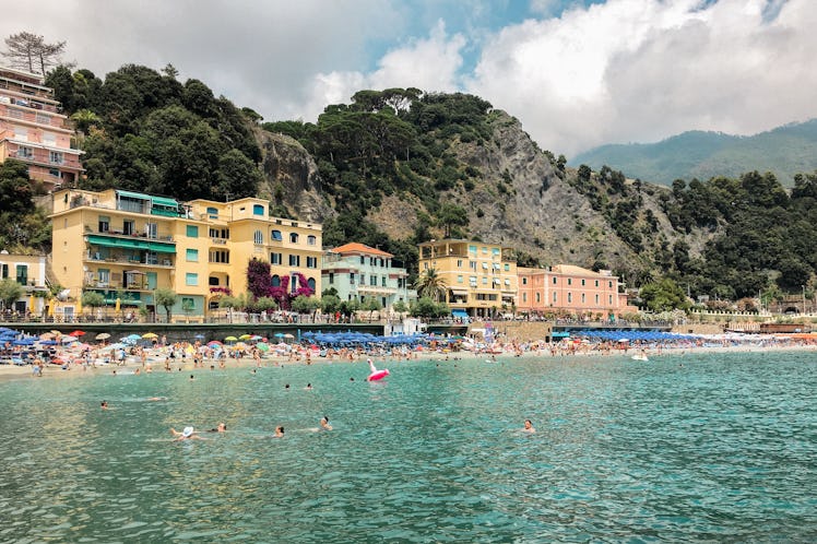 The pastel buildings of Monterosso al Mare sit in the Italian cliffside on a busy afternoon.