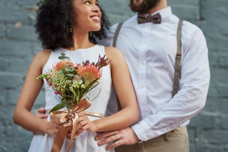 A young couple pose for a picture in front of a light blue after getting married.