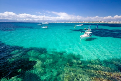 Boats sit in the teal waters off the coast of Mallorca, Spain on a sunny day.