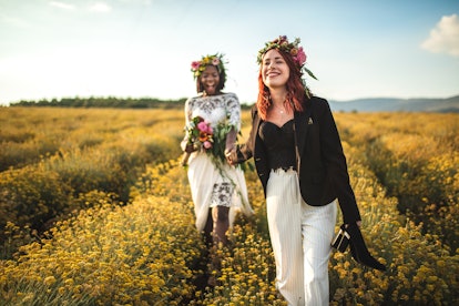 A lesbian couple takes pictures in a flower field at golden hour after getting married.