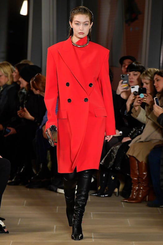 Gigi Hadid wearing a red coat and black leather knee-high boots from Proenza Schouler's Fall/Winter ...