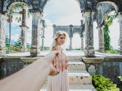 A couple holds hands while walking through ruins in Bali on a sunny day.