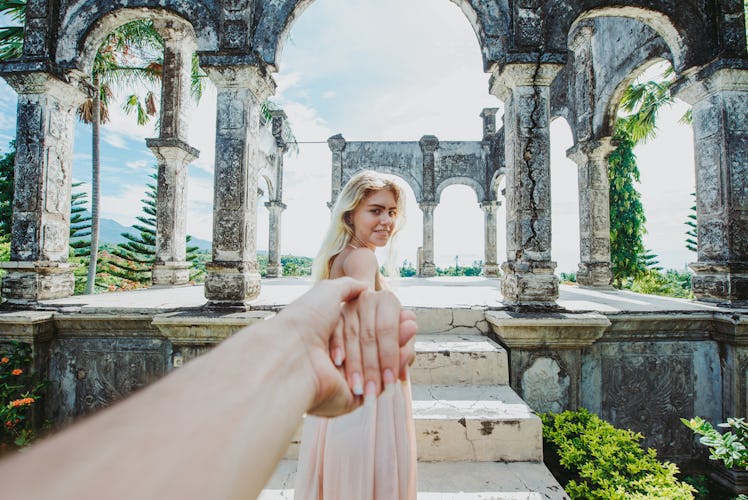 A couple holds hands while walking through ruins in Bali on a sunny day.