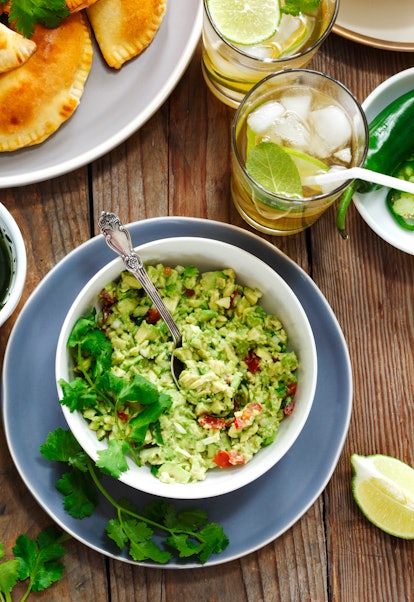 A bowl of guacamole sits on a wood table next to other vegan foods.