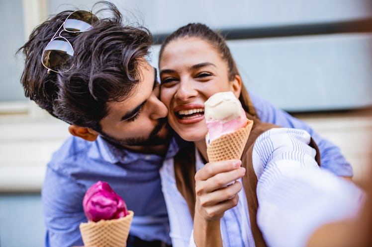 A couple holds up their ice cream cones and poses for a selfie.