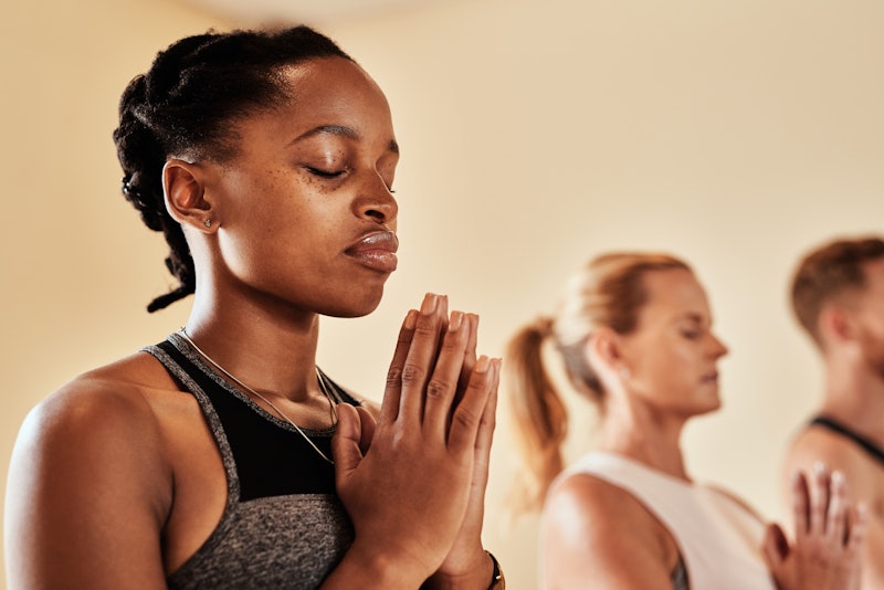 A person sits with her eyes closed in a meditative yoga pose. Meditation before or after a workout c...