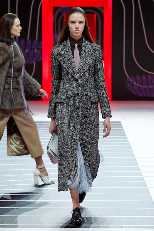 A model walking the Prada Fall 2020 runway in a long grey coat, black blazer and light pink tie