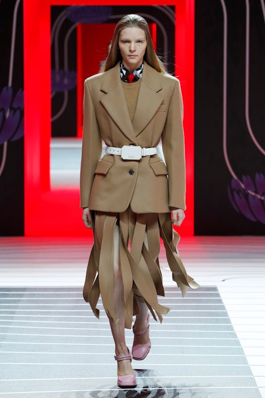 A model walking the Prada Fall 2020 runway in a beige blazer and a beige skirt cut into strands 