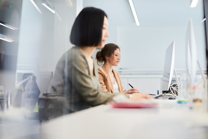 Zwei Frauen sitzen an einem Schreibtisch in einem Großraumbüro und furzen leise. Ein geräuschloser Furz ist eine Art von Blähungen, die etwas über die Gesundheit Ihres Darms aussagen kann