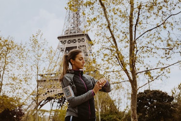 A woman in workout apparel looks at her watch with the Eiffel Tower in the background.