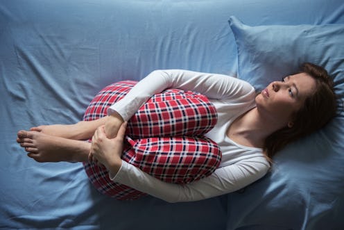 A woman is curled up in bed. Missing periods can be a sign of medical issues or problems like intens...