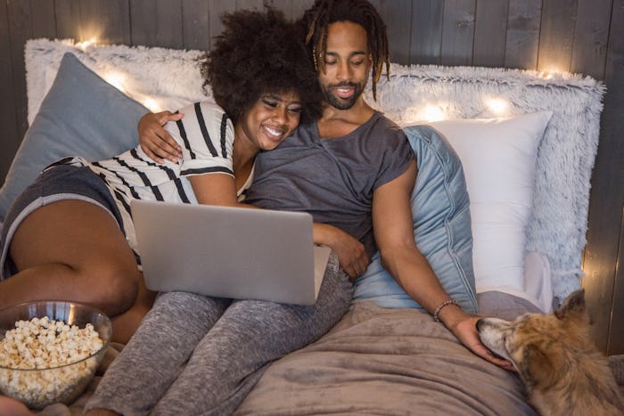man woman in bed eating popcorn with laptop
