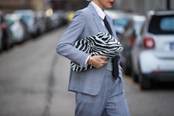 A woman wearing a grey check suit and a zebra print clutch while crossing the street