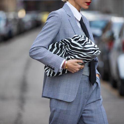 A woman wearing a grey check suit and a zebra print clutch while crossing the street