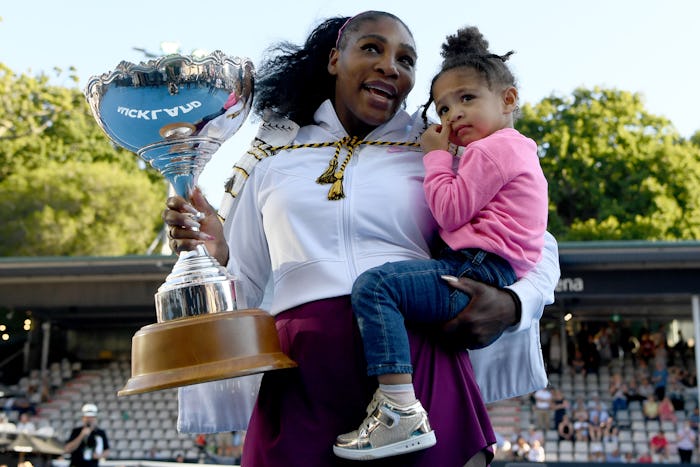 Serena Williams holding a trophy in one hand and her daughter in the other