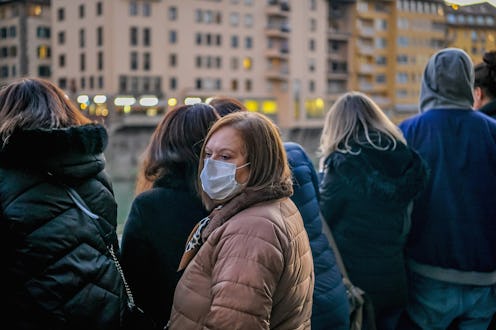 A person stands in a crowded street wearing a mask to filter potential pathogens from the air. The c...
