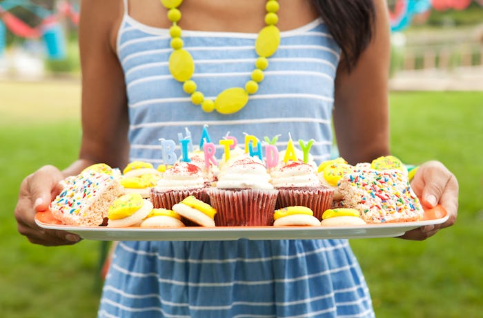 a girl holding a birthday board with cupcakes and other treats