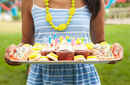 a girl holding a birthday board with cupcakes and other treats