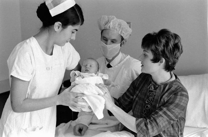 A proud 1969 mom passes her newborn to a nurse and doctor.