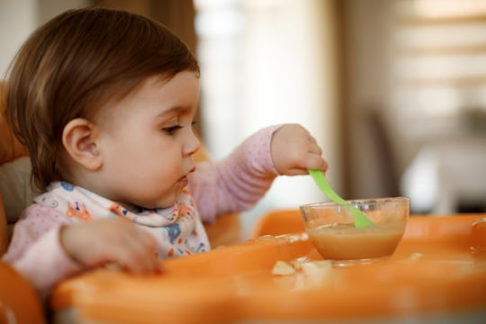 toddler girl sitting at high chair eating applesauce