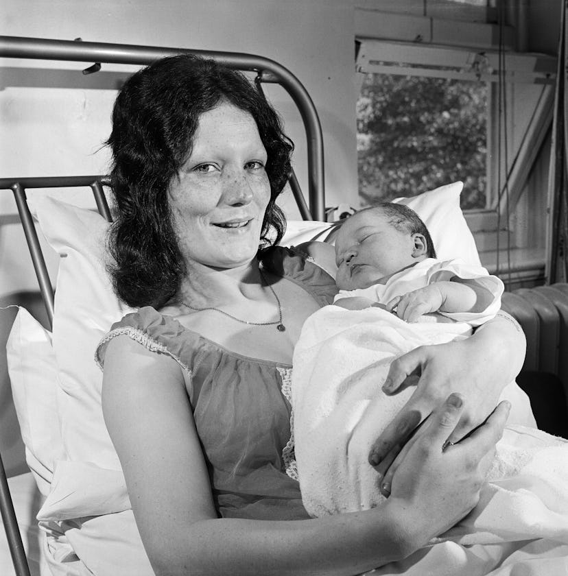 A mom holds her newborn baby with pride in her hospital bed, smiling with tired eyes at the camera.